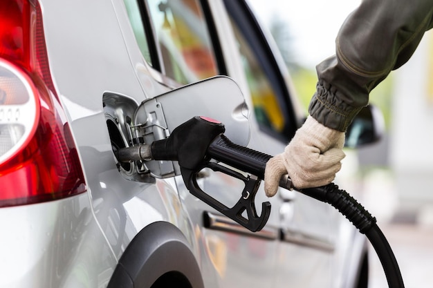 Mão na luva de tecido branco reabastecendo o carro metálico cinza no posto de gasolina fechado com foco seletivo e desfoque