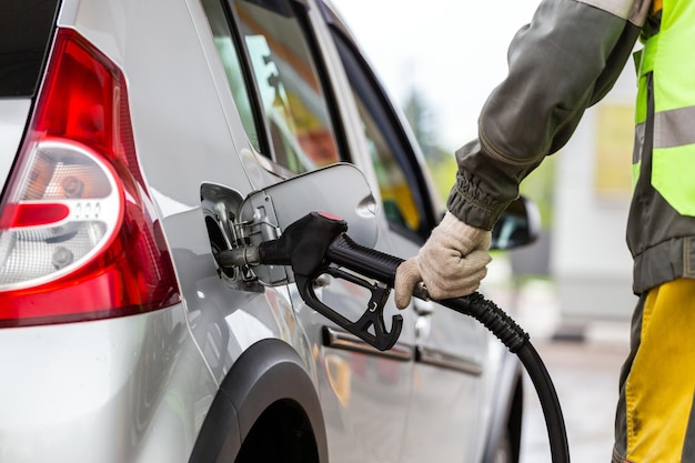 Mão na luva de tecido de algodão branco reabastecendo o carro metálico cinza no fechamento do posto de gasolina com foco seletivo