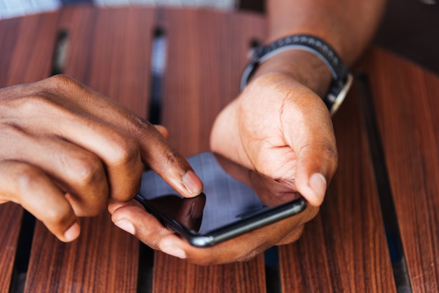 Mão negra segurando um smartphone moderno e tocando a tela em branco com o dedo