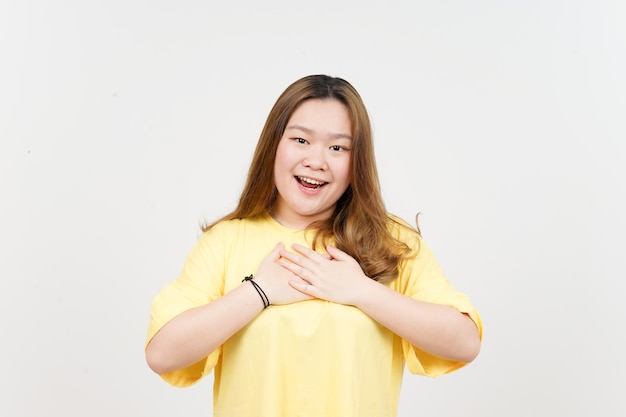 Mão no peito gesto grato de uma linda mulher asiática vestindo camiseta amarela isolada em branco