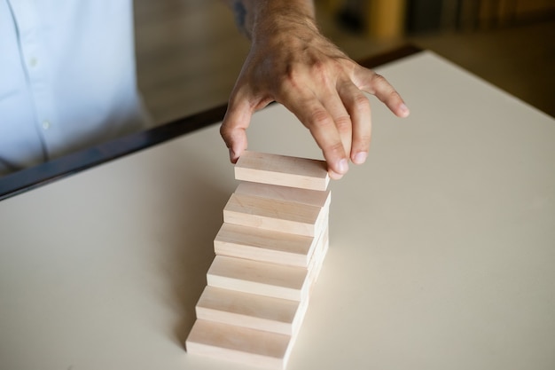 Mão organizando o empilhamento de blocos de madeira como escada de degraus.