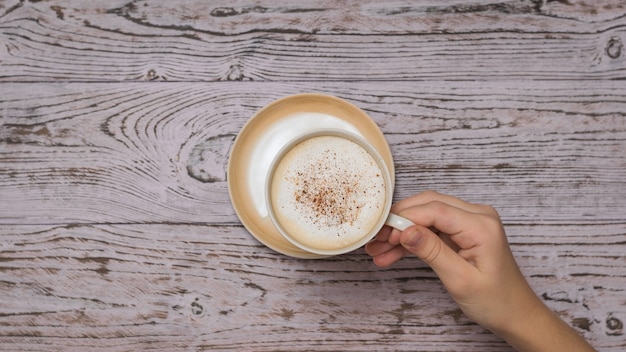 Mão pega uma xícara de café da mesa de madeira