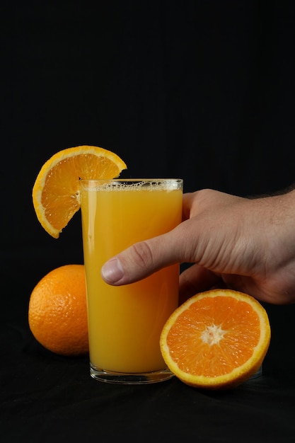 Foto mão pegando um copo de suco de laranja em fundo preto