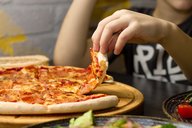 Mão, pegando uma fatia de pizza de pepperoni da bandeja de madeira redonda