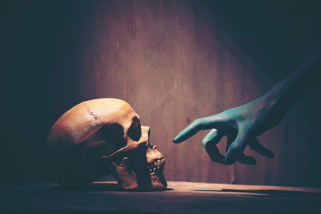 Mão pintada cortada de pessoa apontando para um crânio humano na mesa no escuro