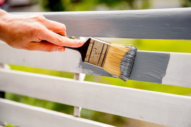 Mão pintando placas de madeira brancas com tinta cinza usando pincel.