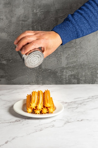 Mão polvilhando açúcar para alguns churros quentes em um prato branco. Doce típico espanhol