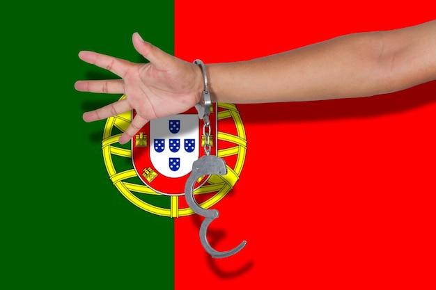 Foto mão recortada de pessoa que usa algemas contra a bandeira portuguesa