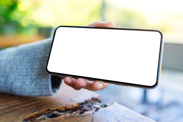 Foto mão recortada de pessoa segurando um smartphone em branco na mesa