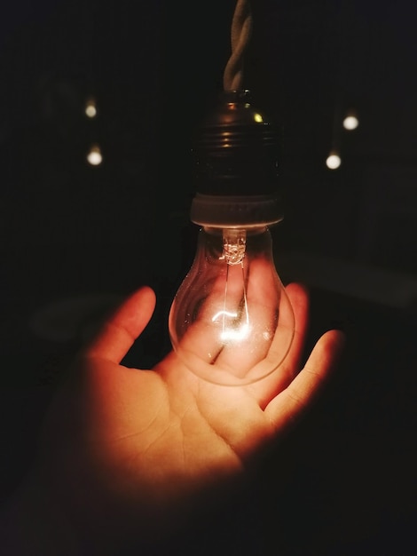 Foto mão recortada de pessoa segurando uma lâmpada iluminada à noite