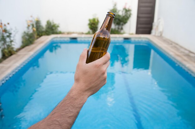 Mão recortada segurando garrafa contra a piscina