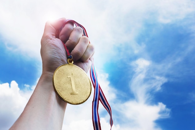 Mão recortada segurando medalha de ouro contra o céu