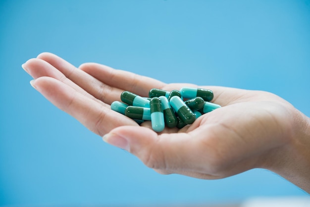 Mão recortada segurando medicamentos em fundo azul