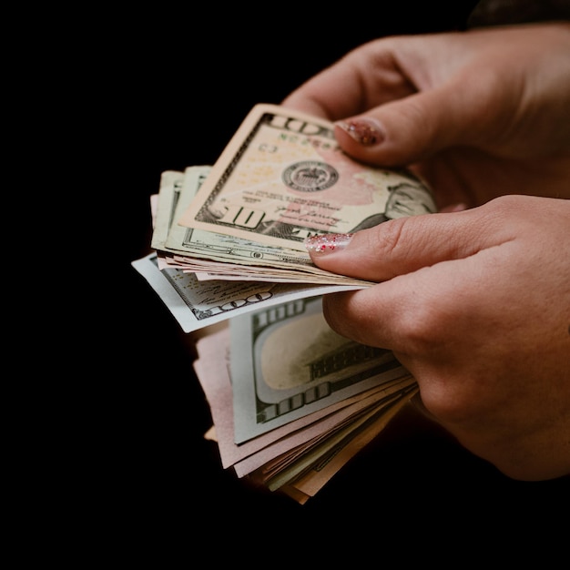 Mão recortada segurando moedas de papel contra fundo preto