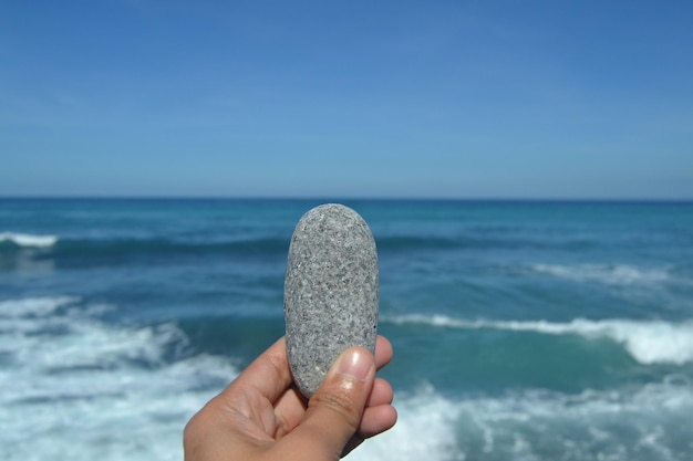Foto mão recortada segurando pedra contra o mar