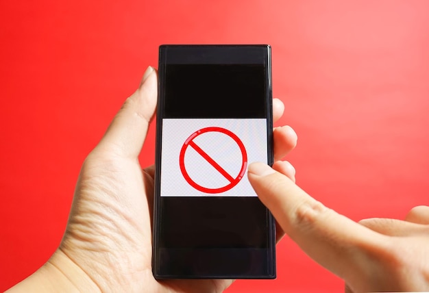 Foto mão recortada segurando telefone celular com sinal de parada sobre fundo vermelho