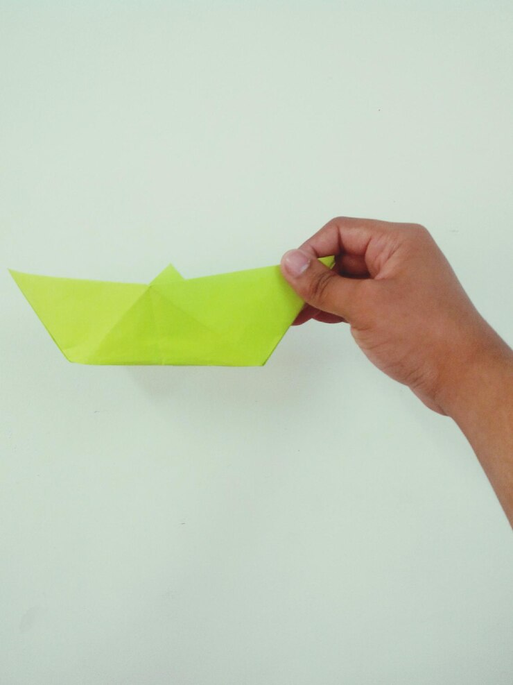 Foto mão recortada segurando um barco de papel contra fundo branco