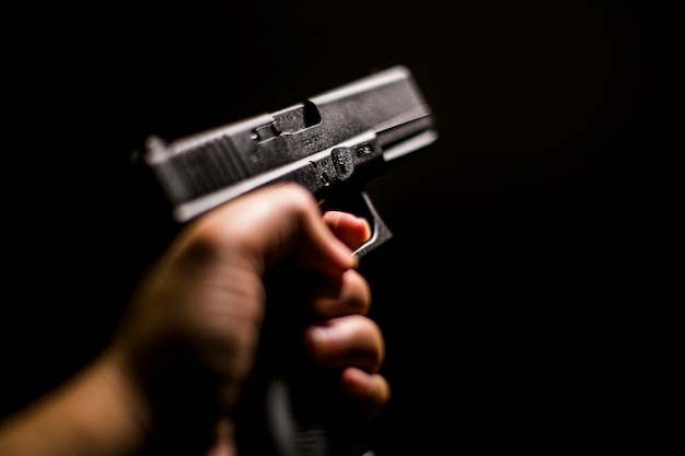 Mão recortada segurando uma arma contra fundo preto