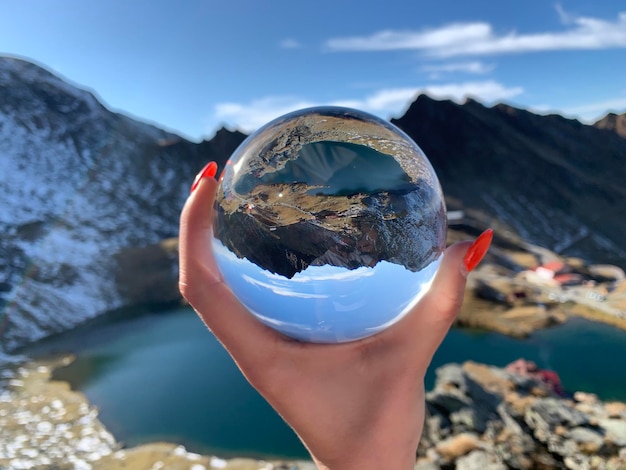 Foto mão recortada segurando uma bola de cristal contra a montanha