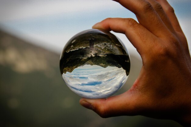 Foto mão recortada segurando uma bola de cristal contra o céu