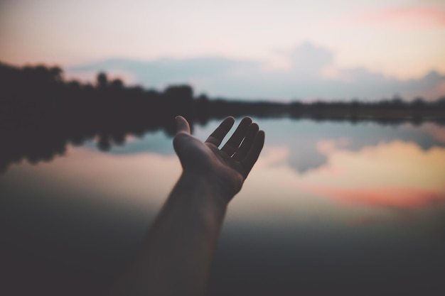 Foto mão recortada sobre o lago contra o céu durante o pôr do sol