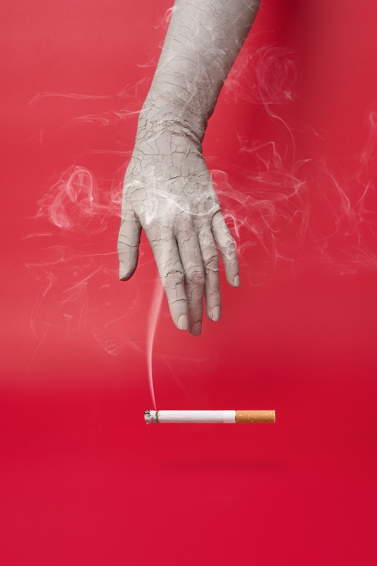 Foto mão seca e rachada e um cigarro fumegante sobre fundo vermelho.
