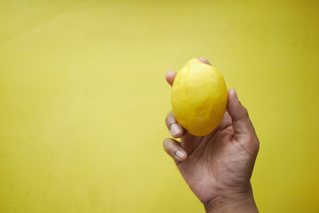 Mão segura limão amarelo em fundo amarelo