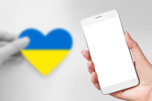 Mão segura um telefone celular com uma tela branca em branco e bandeira ucraniana