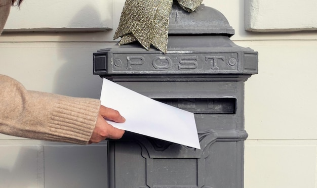 Mão segura uma carta e coloca na caixa de correio antiga perto de casa, entrega de correio