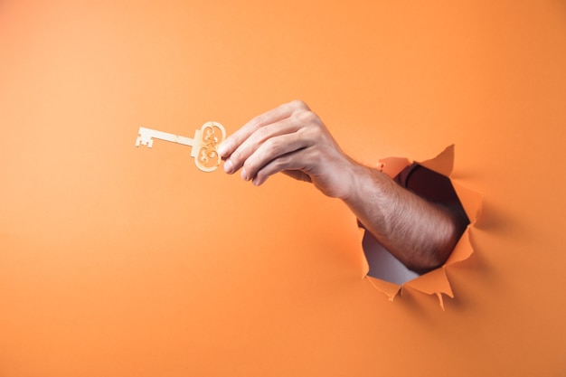 Mão segura uma chave de madeira em um fundo laranja