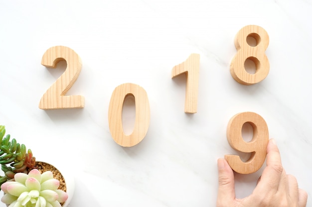 Mão segurando 2019 feliz ano novo letras de madeira no fundo de mármore branco