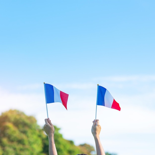 Mão segurando a bandeira da França no feriado de fundo do céu azul do Dia da Bastilha do Dia Nacional da França e conceitos de celebração feliz