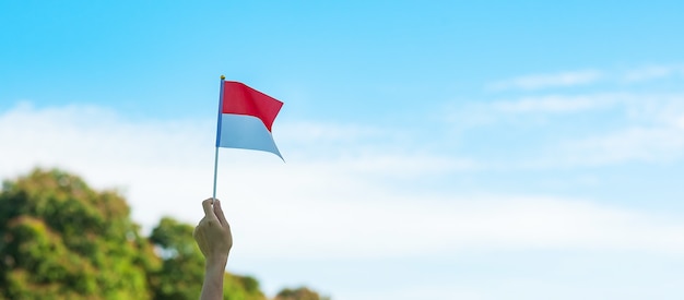 Mão segurando a bandeira da Indonésia no fundo do céu azul. Dia da independência da Indonésia, dia do feriado nacional e conceitos de celebração feliz
