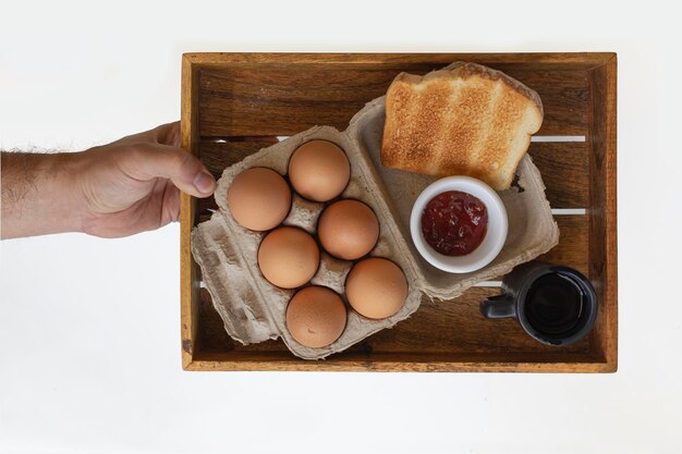 Mão segurando a bandeja de café da manhã americano, ingredientes tradicionais, ovos, geléia e café