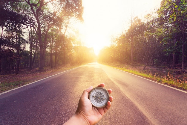 Mão segurando a bússola na estrada de asfalto vazia e no por do sol.