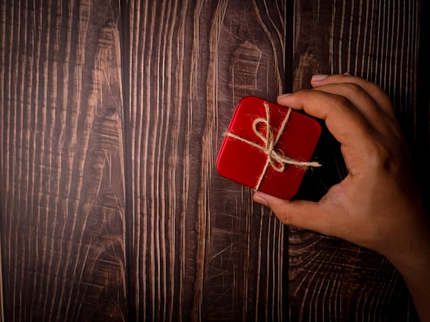 Mão segurando a caixa de presentes vermelha em uma mesa de madeira Feriados fundo de natal Copiar espaço para texto ou design Vista de cima