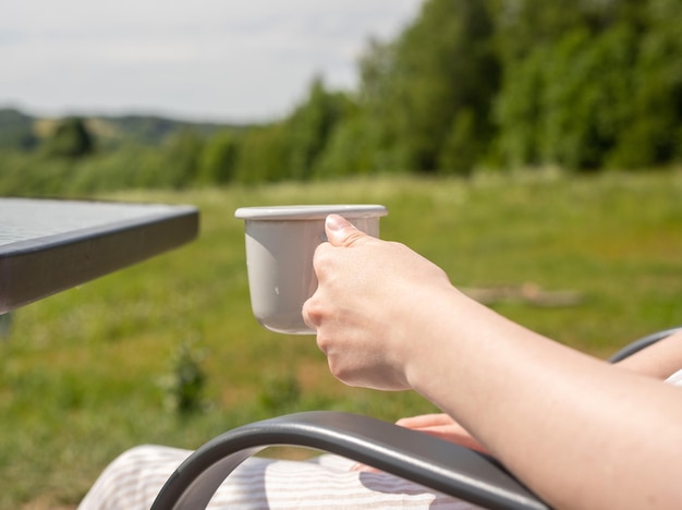 Mão segurando a caneca de xícara de chá na paisagem verde da natureza de verão