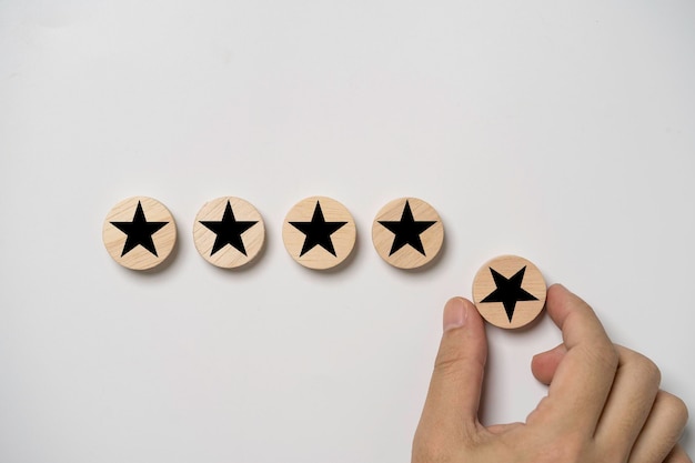 Mão segurando a estrela negra que imprime tela em madeira redonda para dar cinco estrelas para excelente avaliação após o uso do cliente, serviço de produto ISO e conceito de certificado padrão de qualidade