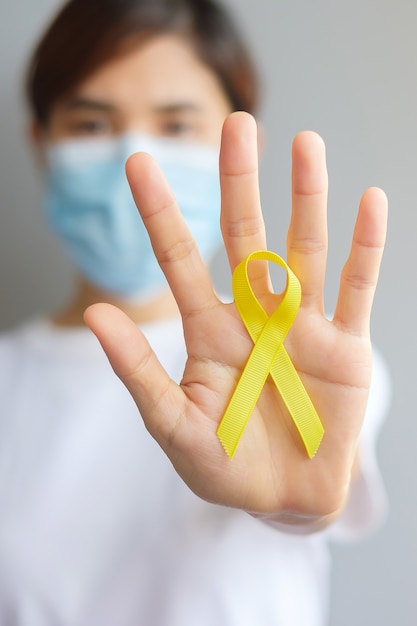 Foto mão segurando a fita amarela para apoiar as pessoas que vivem e doenças. setembro dia da prevenção do suicídio, conceito do mês da conscientização da infância, do sarcoma e do câncer ósseo