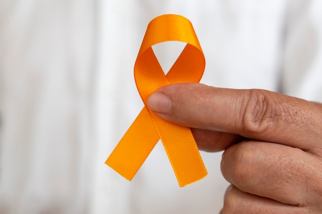 Foto mão segurando a fita laranja. campanha para prevenir câncer de pele, melanoma, laranja de dezembro