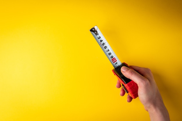 Mão segurando a fita métrica em fundo amarelo.