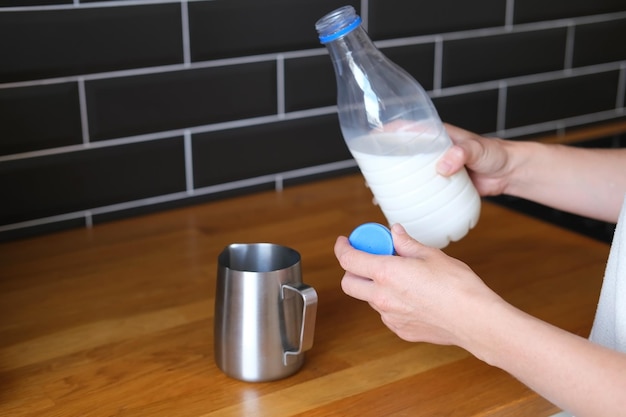 Mão segurando a garrafa de leite e fazendo espuma na jarra de leite