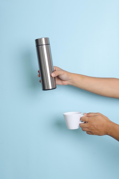 Mão segurando a garrafa térmica de aço inoxidável e caneca para maquete Insira seu texto ou marca