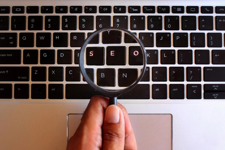 Foto mão segurando a lupa e teclado brilhante com texto seo search engine optimization