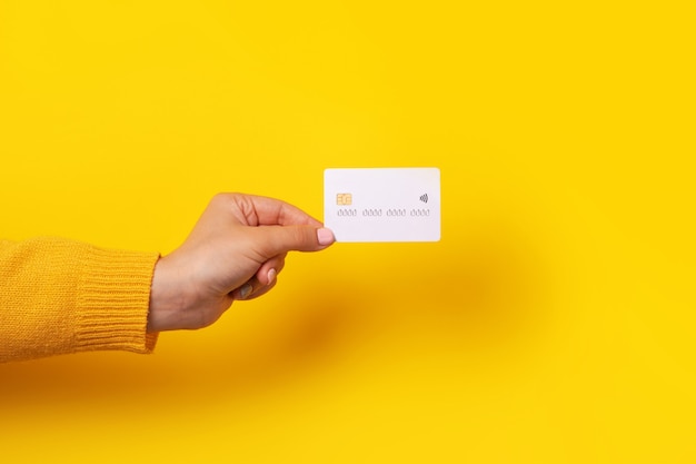 Mão segurando a maquete de cartão de crédito em branco, cartão com chip eletrônico sobre fundo amarelo