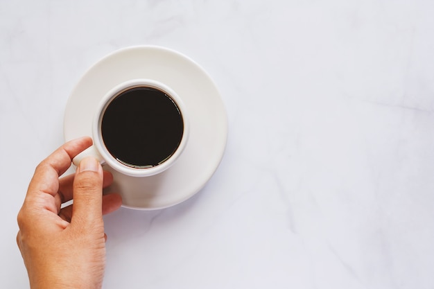 Mão segurando a xícara de café com pires em fundo de mármore branco