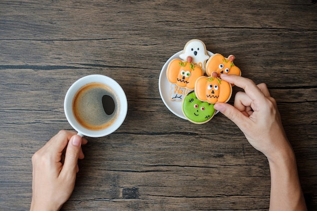 Mão segurando a xícara de café durante comer biscoitos engraçados de Halloween Feliz dia de Halloween Truque ou Ameaça Olá outubro outono outono Festa tradicional e conceito de férias