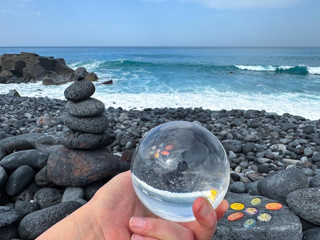 Foto mão segurando bola de cristal pirâmide zen e chakra pedras de cura na costa vulcânica do oceano
