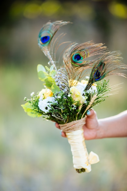 Mão segurando buquê de flores com penas de pavão