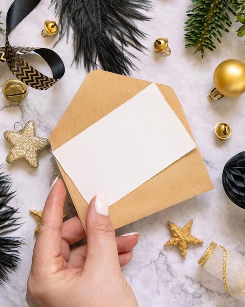 Mão segurando cartão e envelope decorações de Natal pretas e douradas e maquete de ramos de abeto